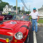 Red classic car with owner posing next to it